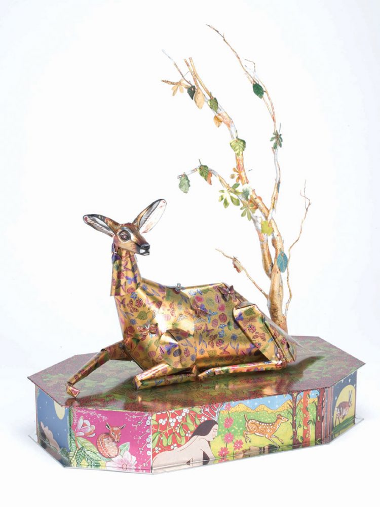 A metal deer sits on top of a metal plinth and underneath a metal tree with various deer imagery and colours printed on to it.