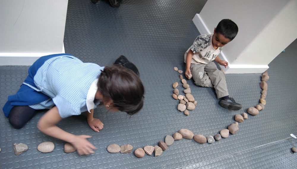 Two children lay out small rocks and pebbles in a curved form.