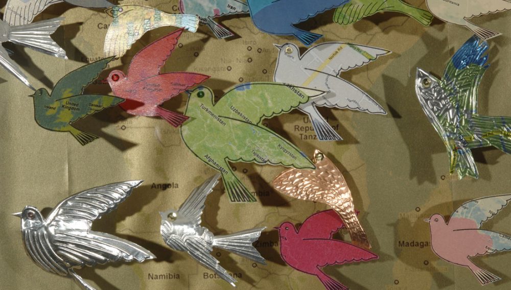 Various birds made out of paper and sheet metal placed on to a map.