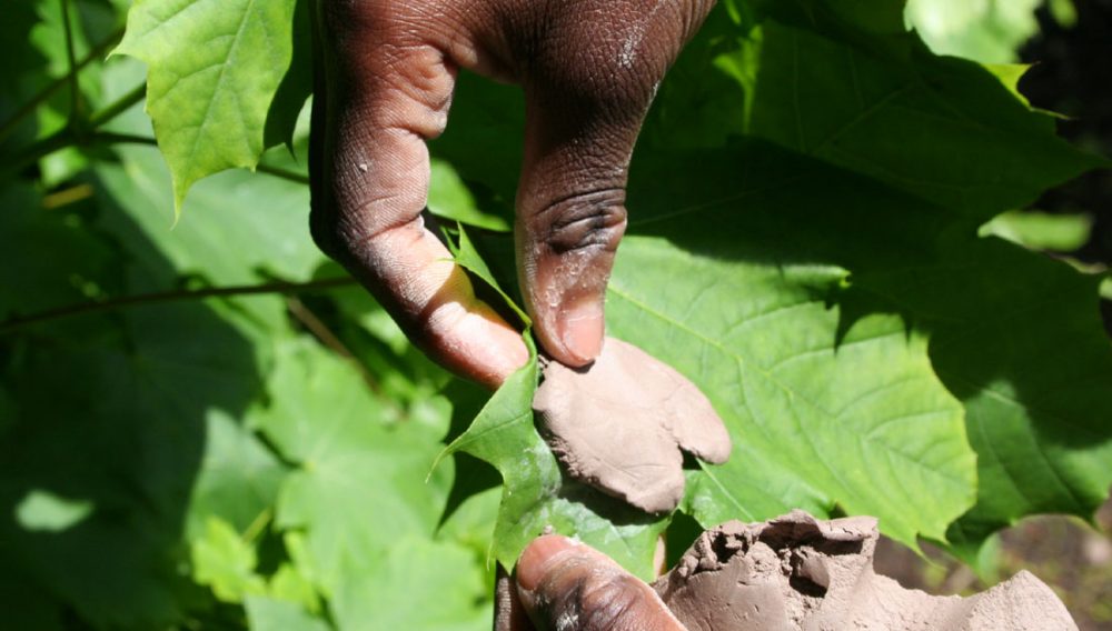 A pair of hands place clay against a leaf to create pattern.