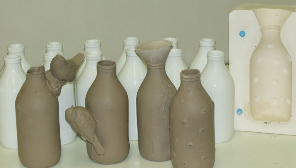 Various ceramic bottles at different stages, some glazed, others clay drying out with the mould next to them.