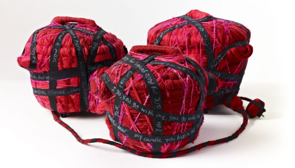 Three pots covered in yarn and thread sit next to each other.