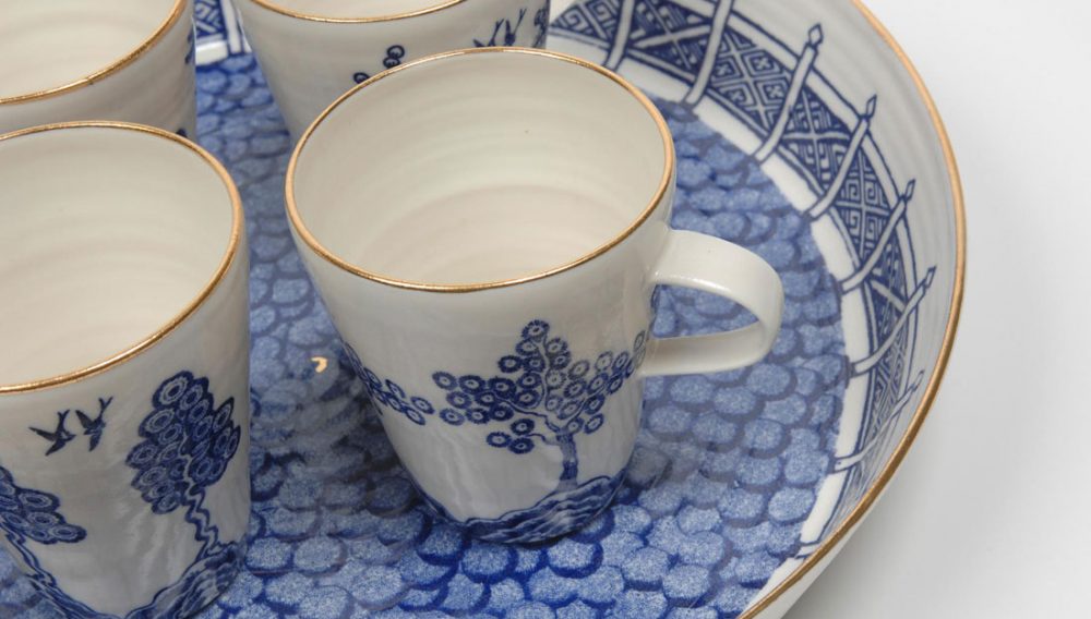 a blue and white teacup with a gold rim sits on top of a bowl which is blue and white with a gold rim.
