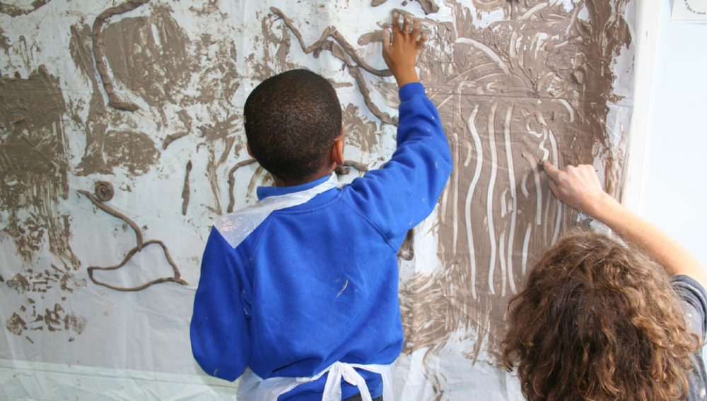 A child uses clay and his hands to create line drawings on the wall.