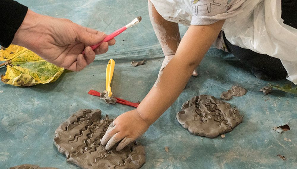 a young hand pushes into wet clay.