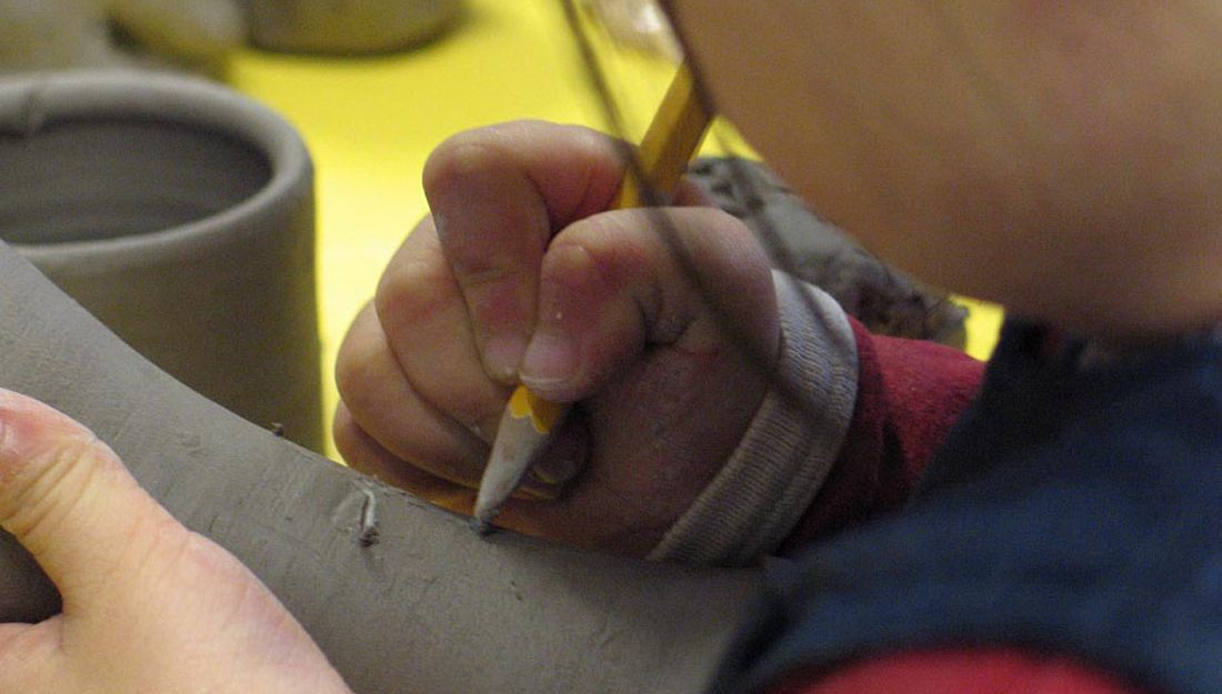 A very young child makes marks in clay using a pencil.