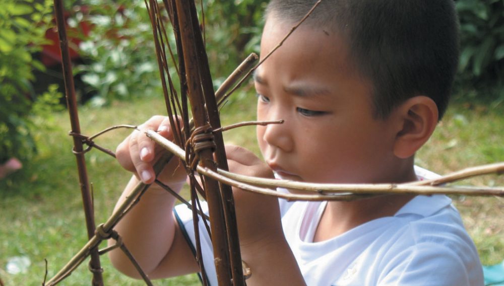 A young boy concentrates on joining two pieces of willow together.