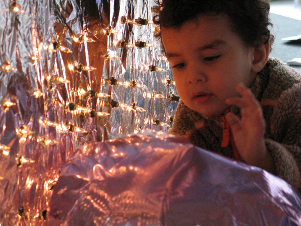 A young child crawls through a tunnel of lights and reflective fabrics.