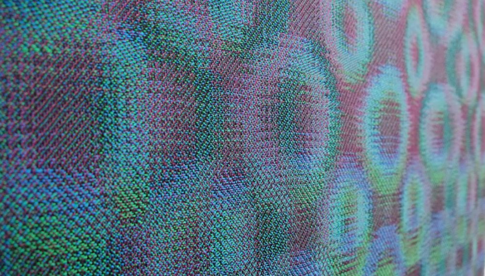 a close up of a contemporary woven hanging. it has a geometric circular design.
