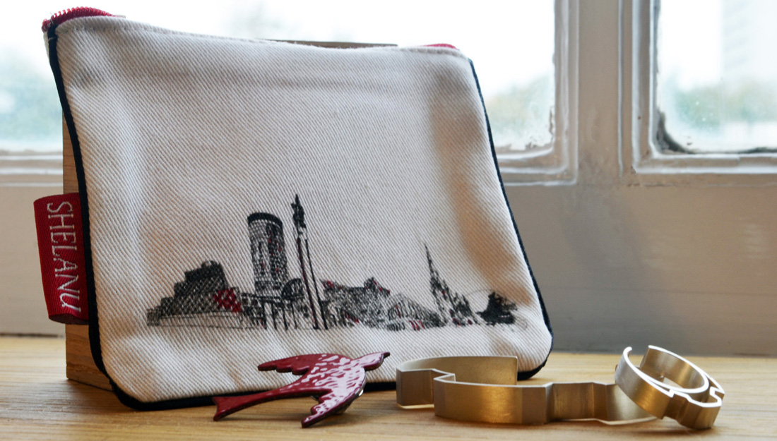 Shelanu products: A purse with a line drawing of Birmingham, a red bird brooch and a silver bracelet.