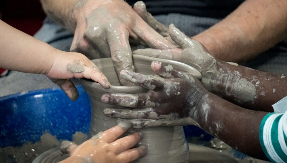 Hands work together on a potters wheel.