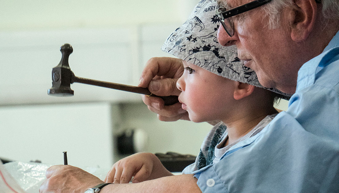 A older man teaches a child how to use a hammer and nail.