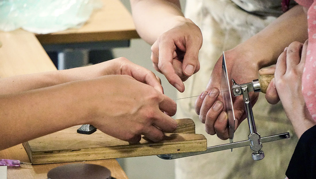 Hands helping an individual place the blade into a piercing saw.