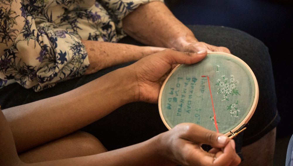 Hands embroidering on to material using an embroidery hoop.