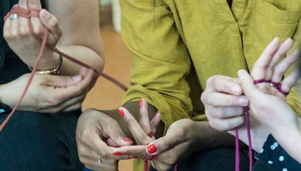 Multiple people use their hands to finger knit with yarn.