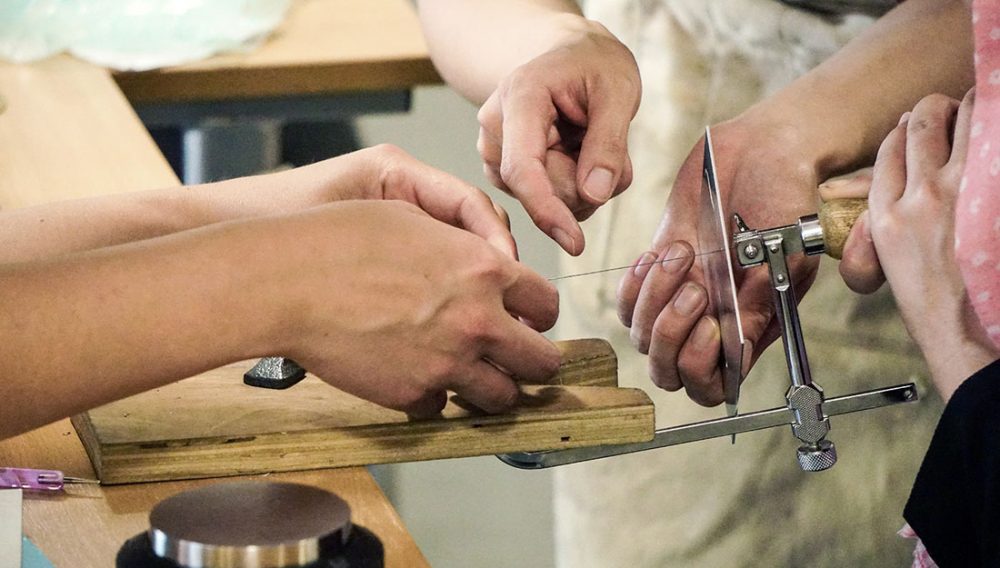 Hands use a piercing saw to cut metal.