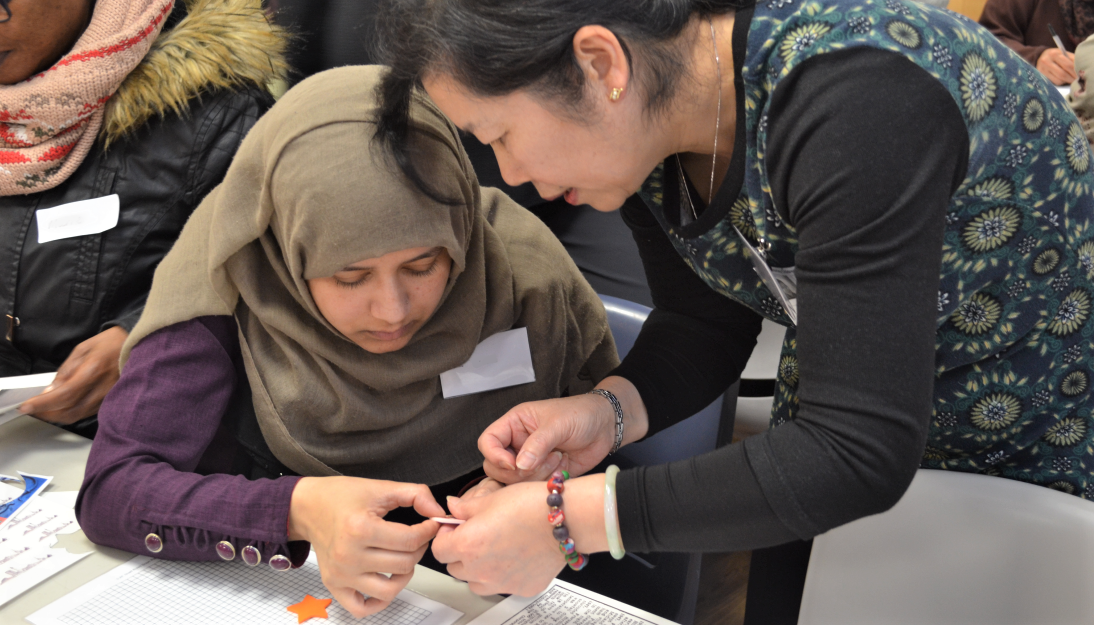 A member of Shelanu helps a lady to make her brooch