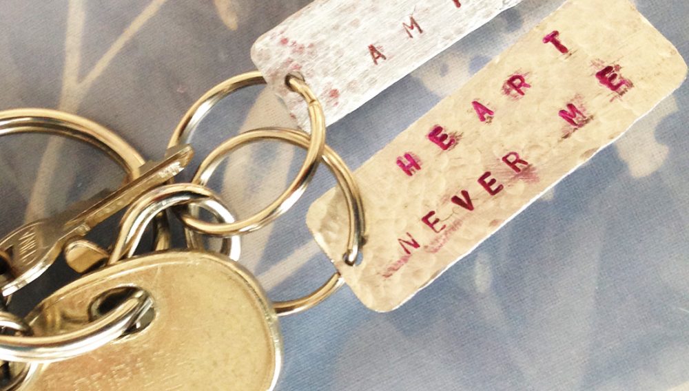 A handmade aluminium key ring with letters stamped on in pink.