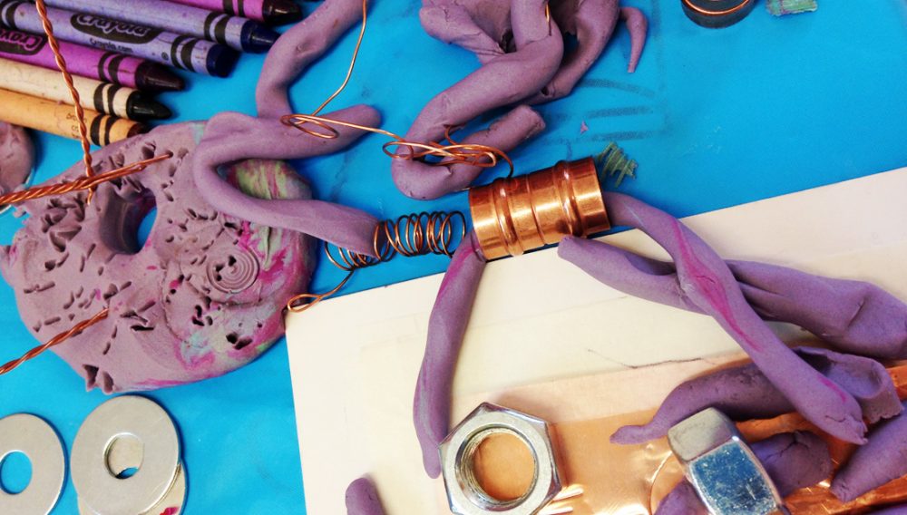 Materials lying on a table including purple clay, copper tubing and crayons.