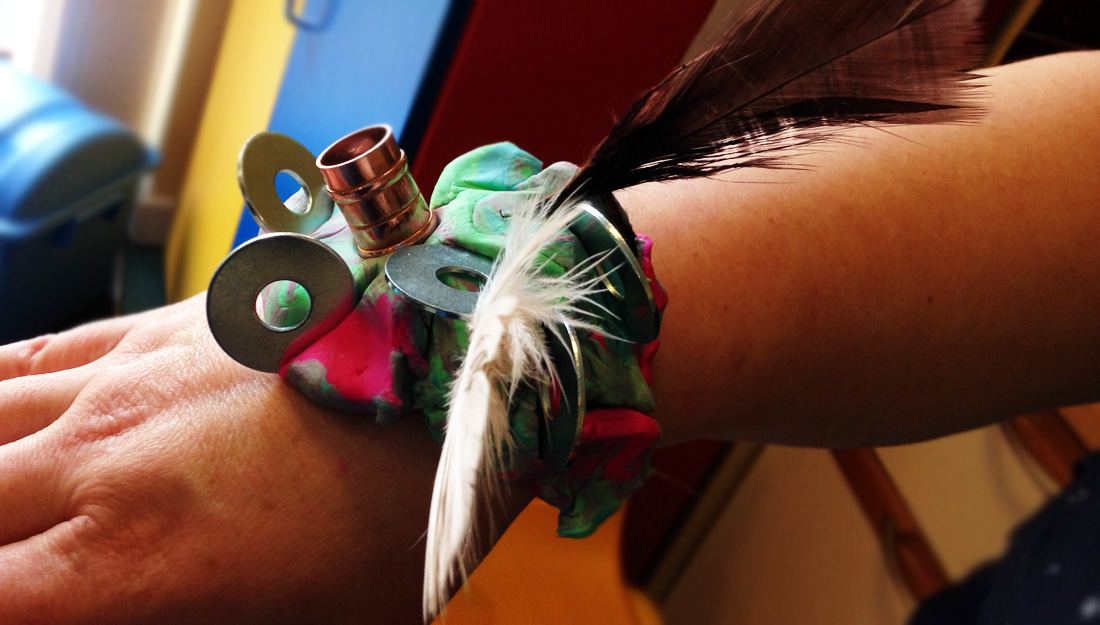 Wrist adornment made with feathers, fabric, copper tubing and washers on a wrist.
