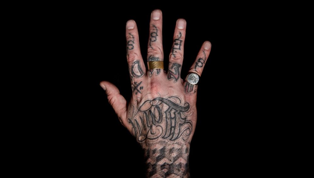 A heavily tattooed hand with rings.