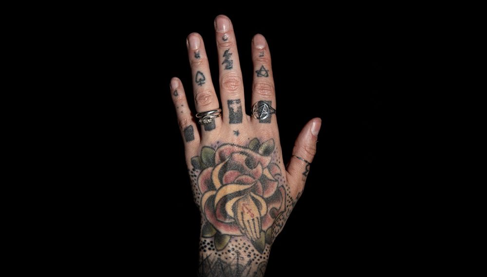 A heavily tattooed hand with rings.