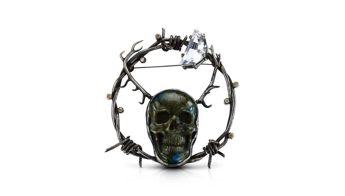 A metal brooch designed with motifs of barbed wire and a skull.