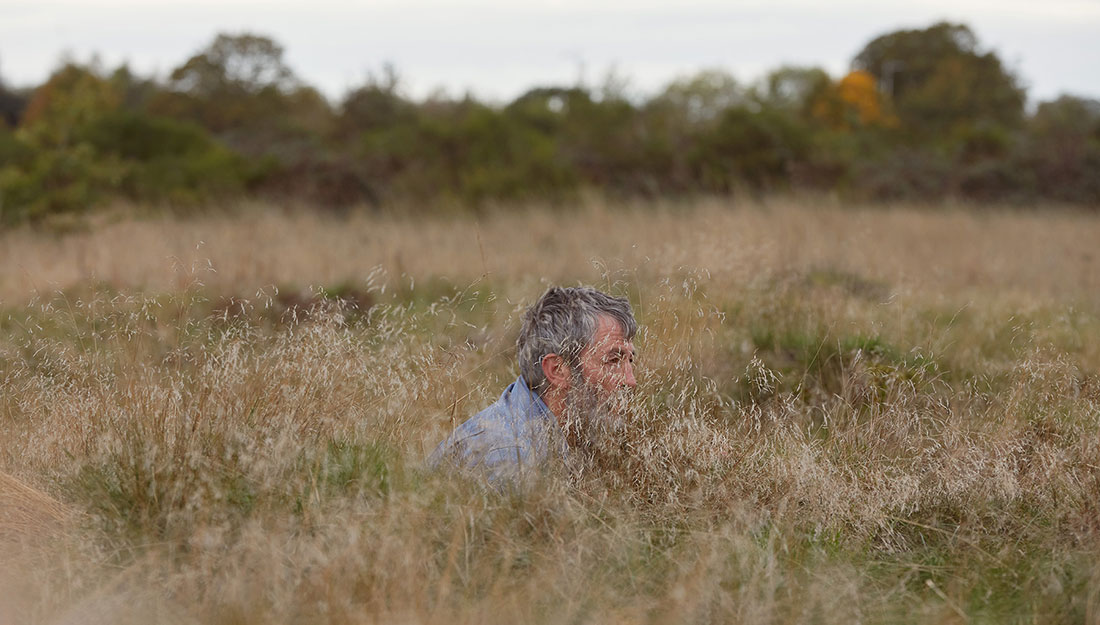 The artist, a middle aged man, crouches in the very long grass.