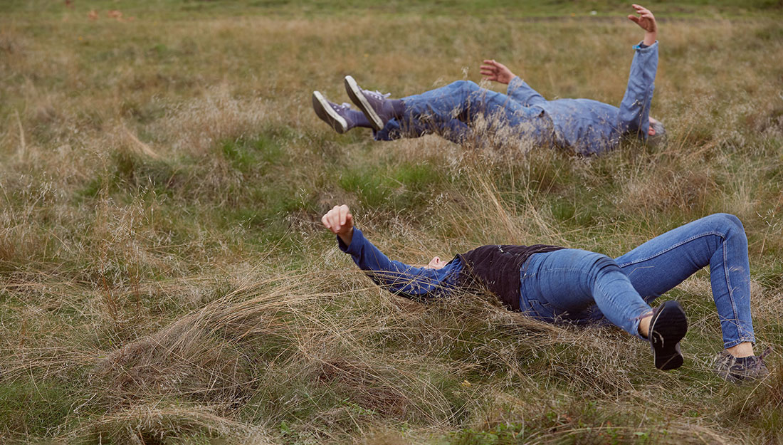 Rehearsing the dance. Two adults roll in the long grass, their legs and arms in the air.