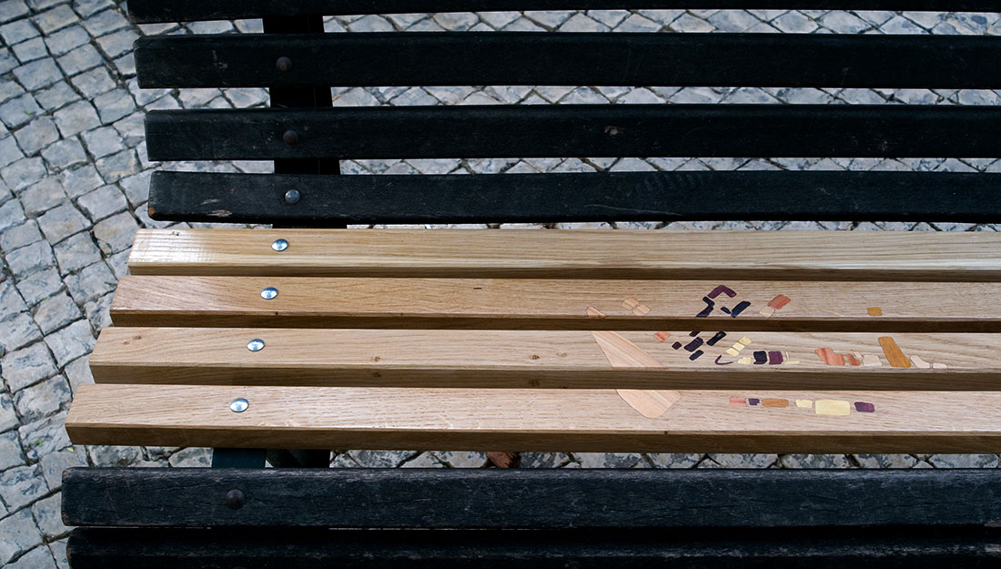 A public bench which has been repaired with new wooden slats and inlaid decoration.