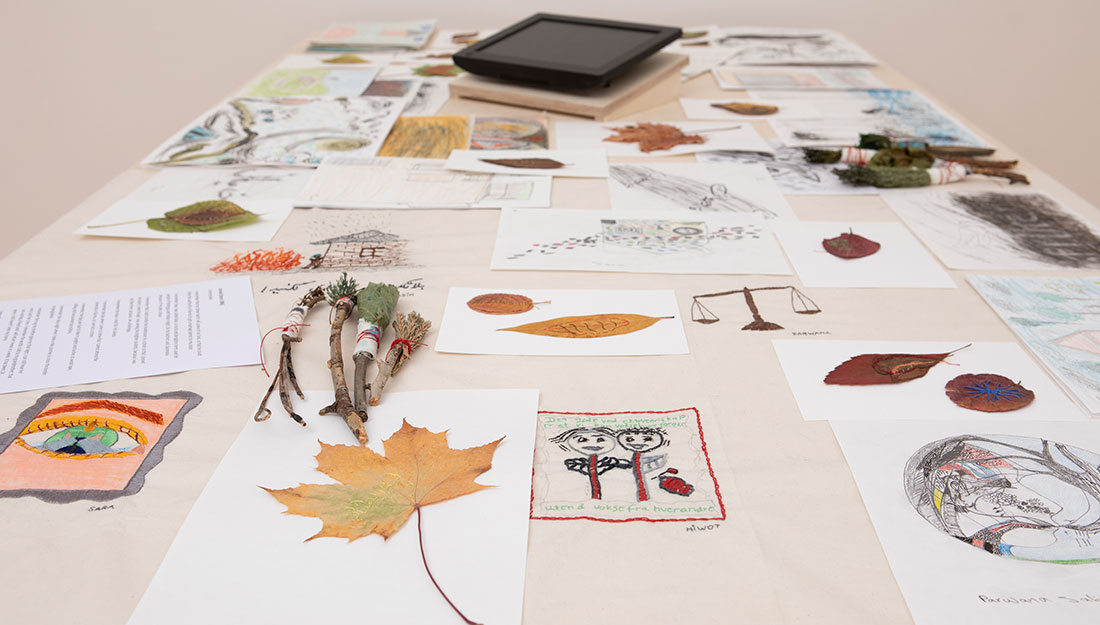A large table is covered with leaves, paper, drawings and brushes made from twigs.