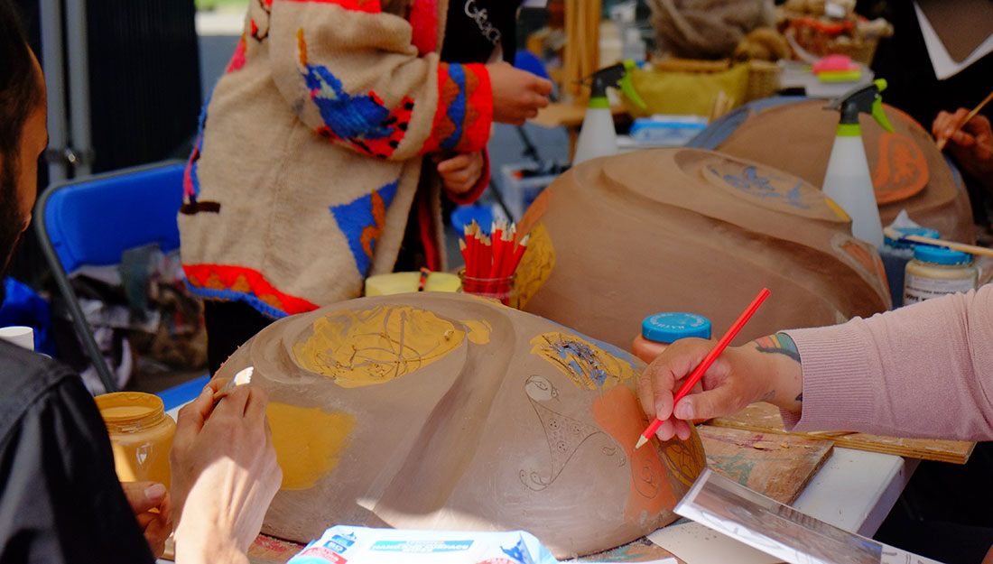 Workshop particpant hands are visible working on creating patterns into large clay forms