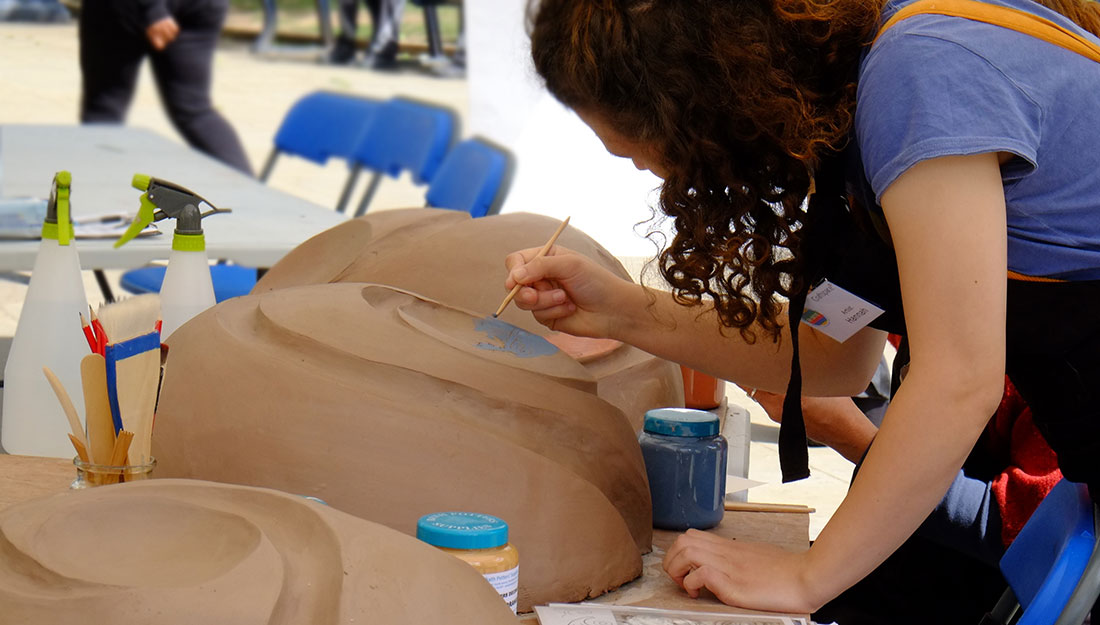 A woman leans over one of three large clay structures with a paintbrush