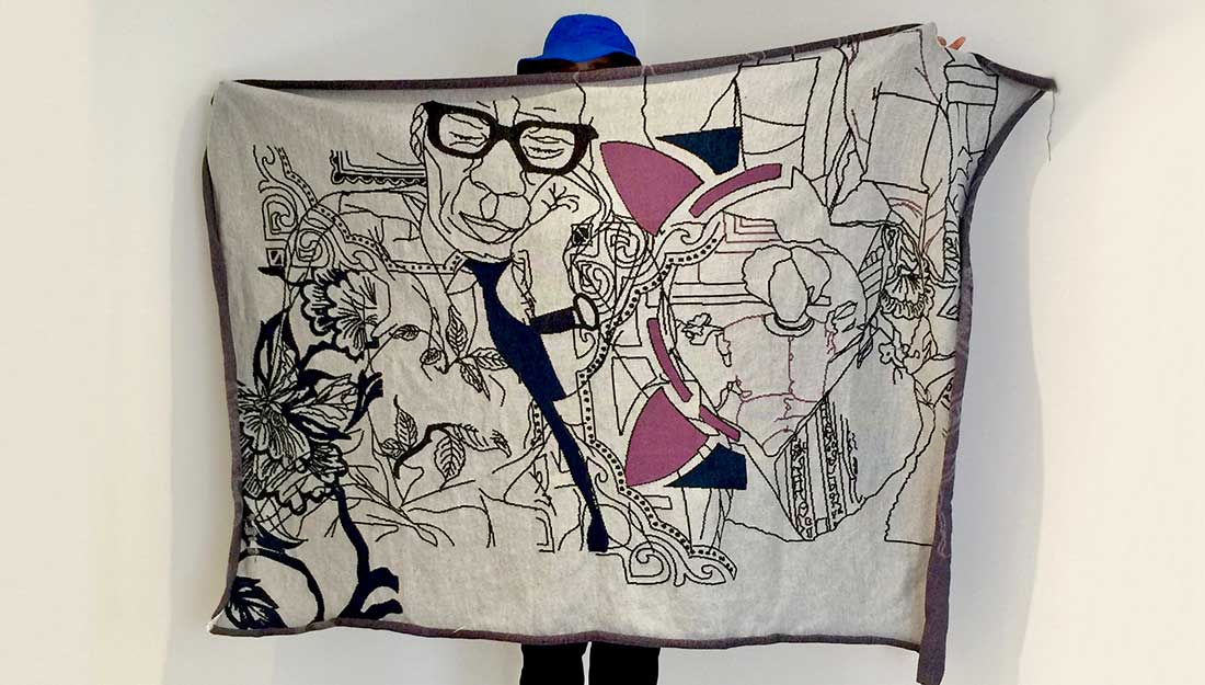 Holding a large textile scarf decorated with images of people.