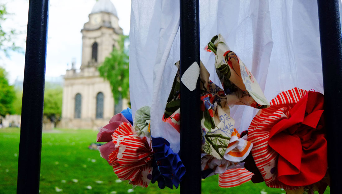 The hem of a dress decorated in colourful fabric applique viewed through a railing with a cathedral in the background