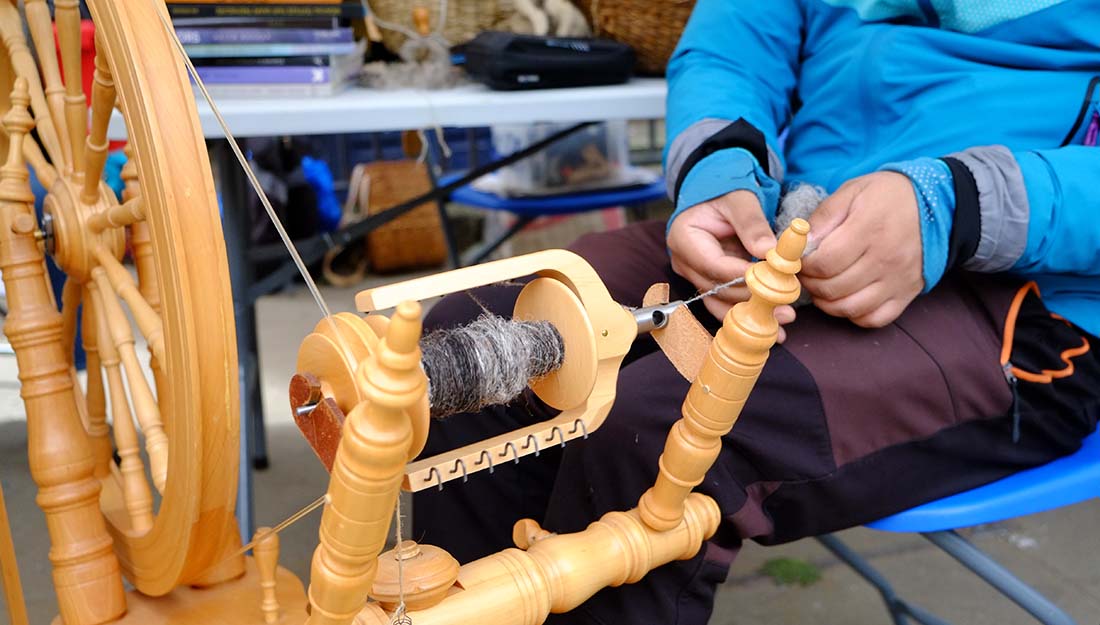 A man sits at a spinning wheel creating his own spool of yarn