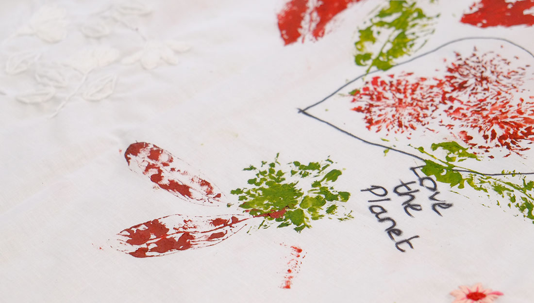 a close up of red and green hand printing onto white fabric with the words Save the Planet visible