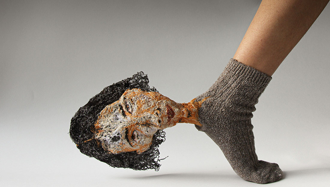 A sock with a textile embroidered head protruding from the heel.