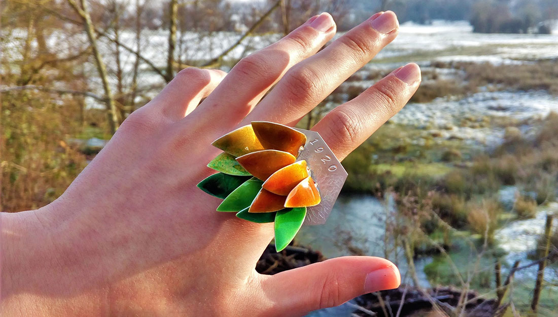 A hand with a large ring made of bright feather or leaf shapes.