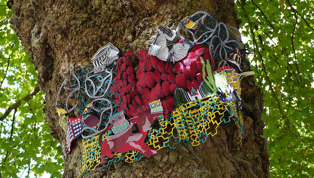 An embroidered artwork of Birmingham landmarks is displayed on a treetrunk.