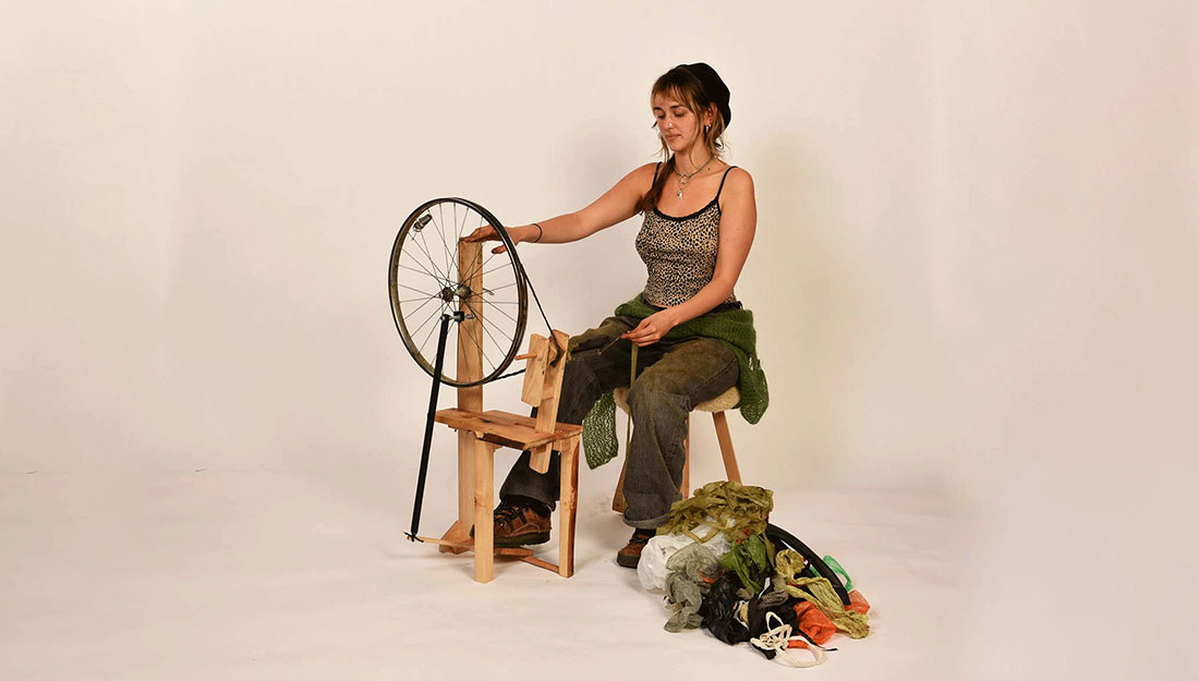 a woman sits at a homemade spinning wheel made from upcycled materials.