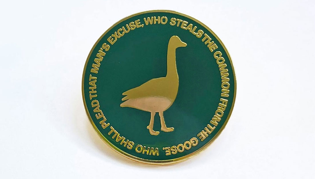 A dark green enamel badge with and golden silhouette of a goose.