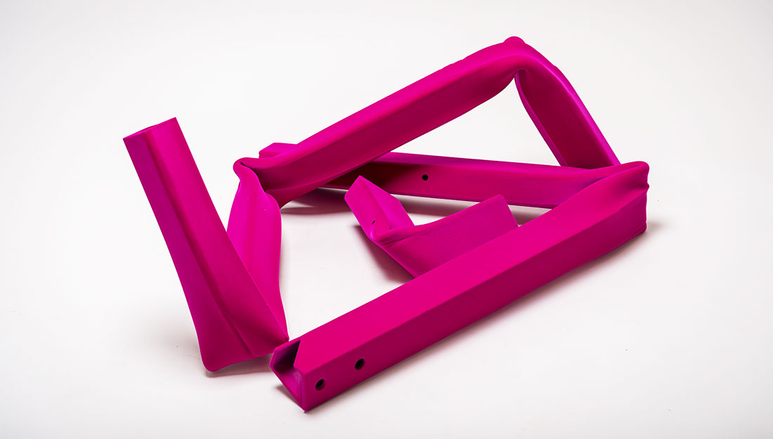 A bright pink abstract form which looks like a bent metal square pole folded over and mishapen.