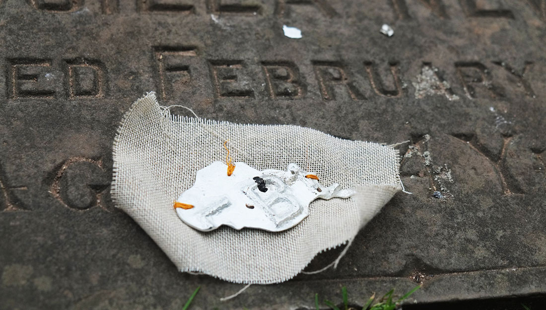 A brooch made from a cast of a letter on a memorial stone. it is stitched to some hessian.
