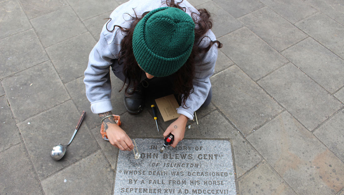 The artist crouches over a memorial stone as she takes a casting.