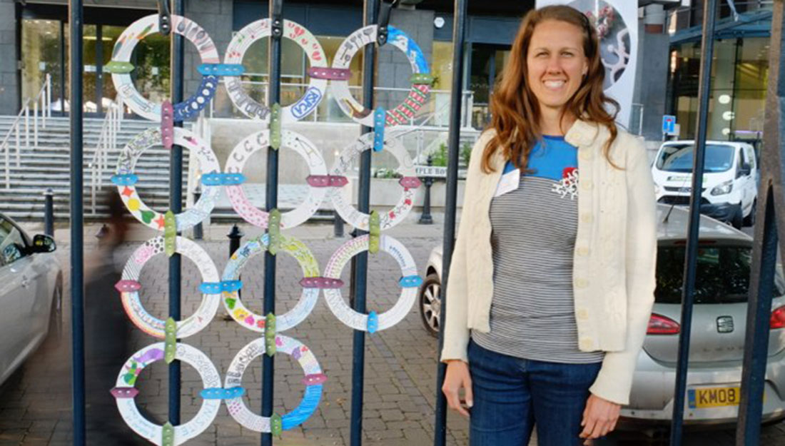 The artist stands next to her artwork, which is hanging on a fence outside.