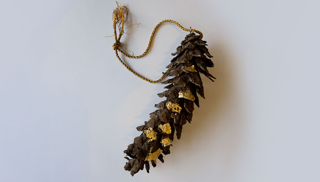 A pine cone with gold decoration on a string.