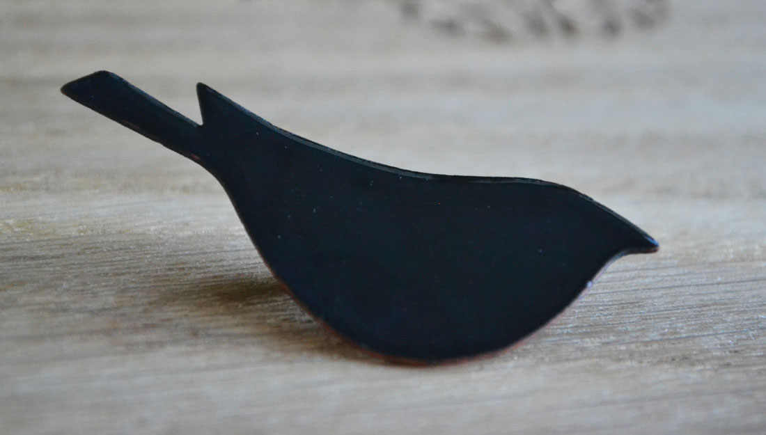 A black solid metal brooch in the shape of a sparrow.