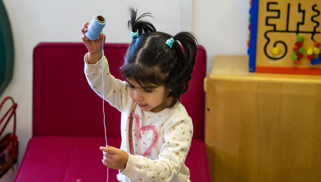 A toddler holds a spool of yarn and concentrates on the dangling thread.