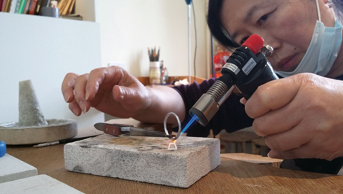 A chinese woman is soldering a silver ring.